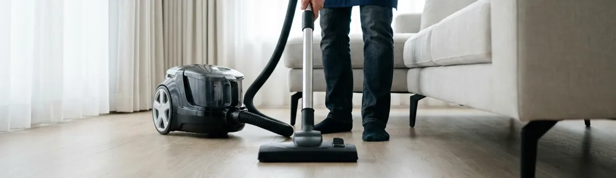 Professional house cleaner vacuuming a living room floor with a canister vacuum cleaner, Boca Raton, FL.