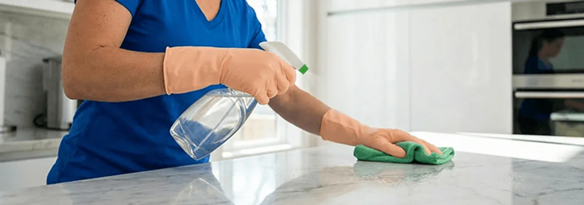 Maid service worker spraying and wiping a kitchen countertop with a microfiber cloth for sanitizing, Boca Raton, FL.